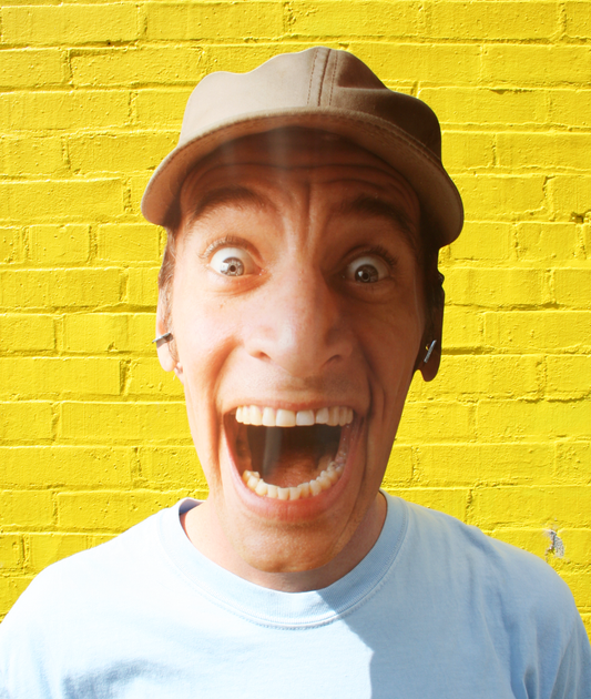 A person wearing an Ernest P Worrell mask with a surprised expression, in front of a yellow brick wall.