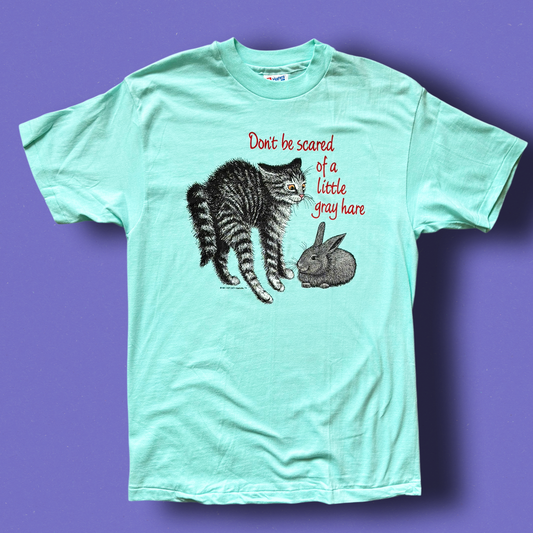 A green t-shirt with a graphic print of a cat and a rabbit, and the text 'Don't be scared of a little gray hare'. Vintage Hep Cat Tee