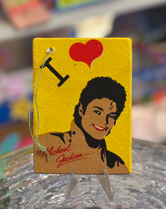 A vintage air freshener featuring an illustration of Michael Jackson with a yellow background, a red heart, and the text 'I ♥ MICHAEL JACKSON'. The item is in original, unopened plastic packaging.