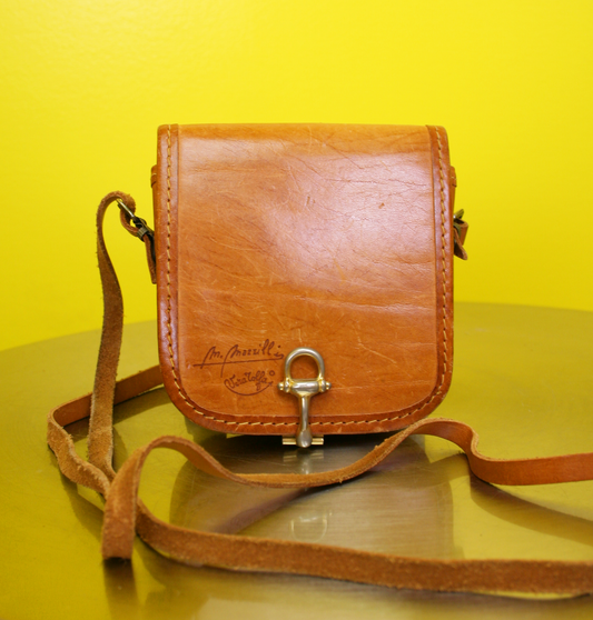 A vintage M. Mazzilli Vera Tolfa mini leather crossbody bag with a tan color and adjustable strap, displayed against a yellow background.