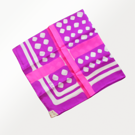 A vibrant silk scarf with a pattern of white spots on a pink background, with a rolled hem.