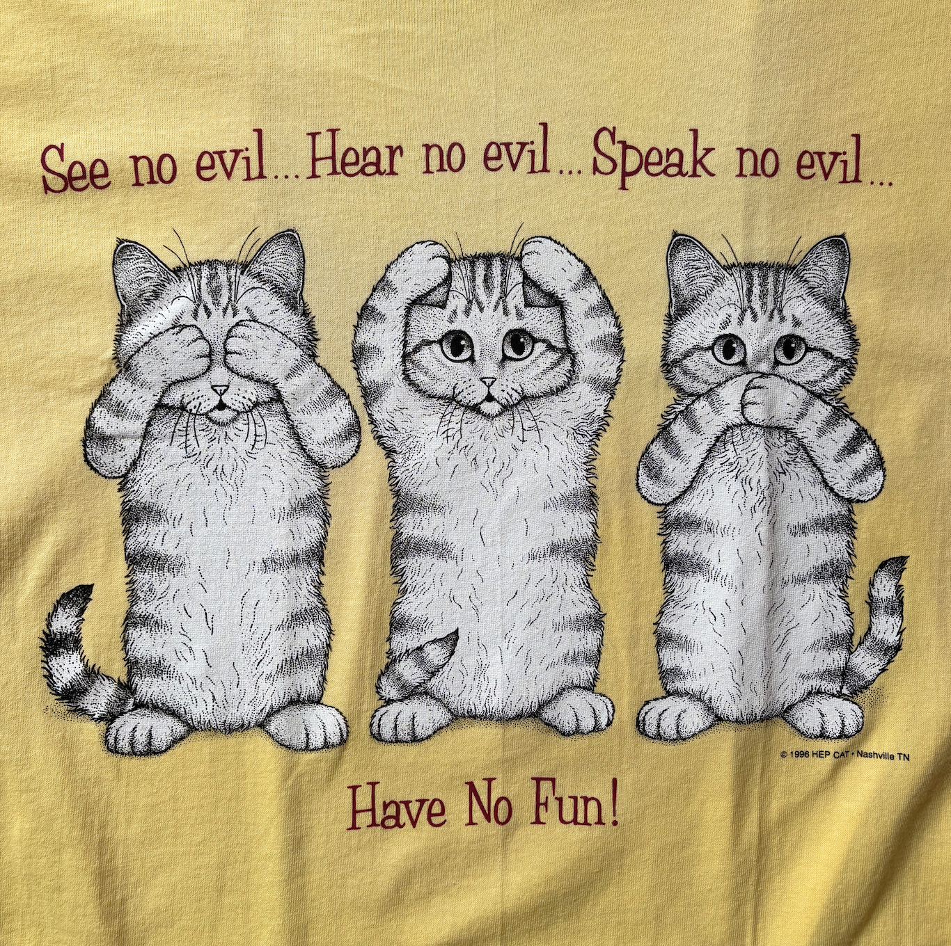 A yellow t-shirt with a graphic print of three cats and the text 'See no evil, Hear no evil, Speak no evil, Have No Fun!'
