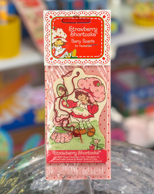 A Strawberry Shortcake hanging air freshener with the character Strawberry Shortcake depicted on the packaging.