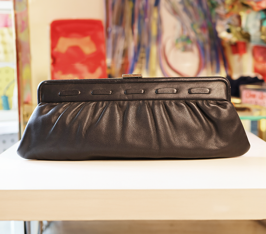 Black clutch bag on a white surface with a colorful abstract painting in the background
