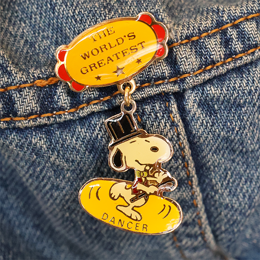 Gold dog character pin on denim fabric with 'The World's Greatest Dancer' text
