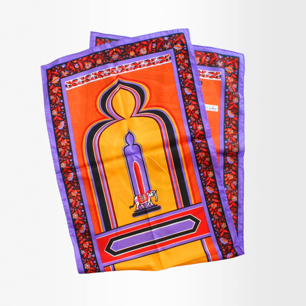 A silk scarf with a bold, colorful 'Elephant' print design, featuring orange, purple, and yellow tones with a geometric patterned border.