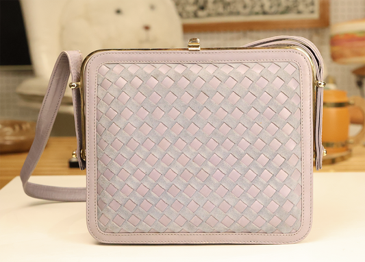 A vintage suede shoulder bag with a basketweave design, featuring a structured silhouette, a kiss-lock top, and gold-tone hardware.