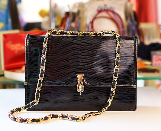 Black handbag with gold chain strap on a table with a blurred background