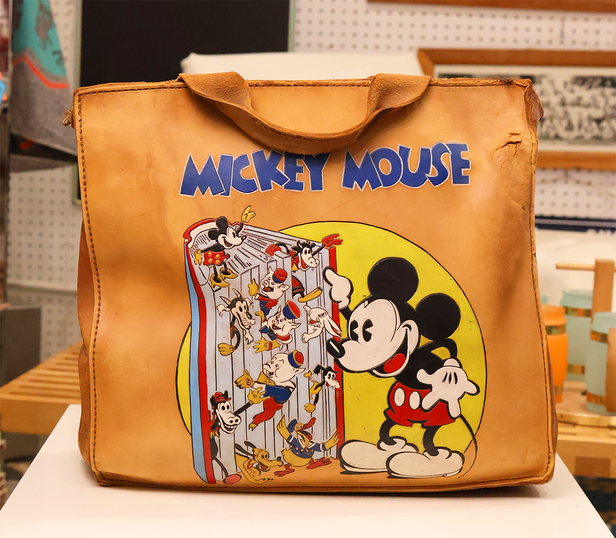 A brown leather hand-tooled and painted messenger bag featuring a vibrant graphic of Mickey Mouse and friends.