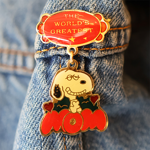Enamel pin with Snoopy and 'The World's Greatest Mom' text on denim fabric