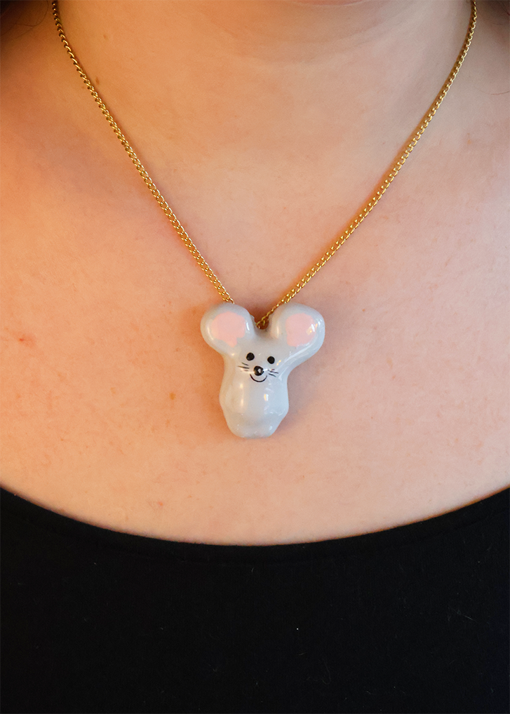 A person wearing a ceramic pendant necklace shaped like a mouse on a gold chain.