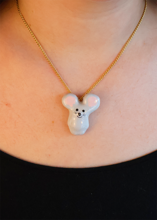 A person wearing a ceramic pendant necklace shaped like a mouse on a gold chain.