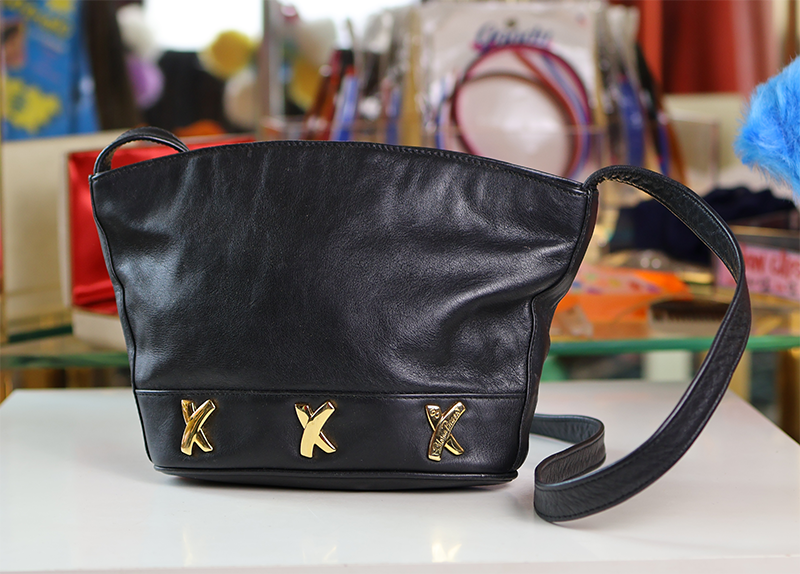 A black leather handbag with gold-colored decorative details on the front and a shoulder strap.