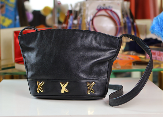 A black leather handbag with gold-colored decorative details on the front and a shoulder strap.