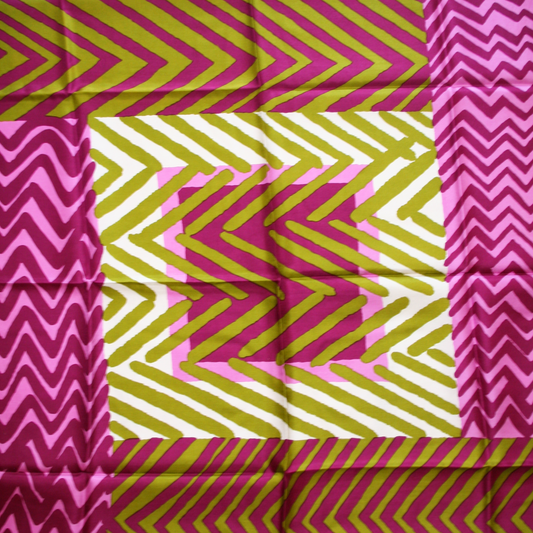 A close-up of a silk scarf with a geometric pattern in vibrant colors, featuring pink, green, and yellow stripes on a white background.