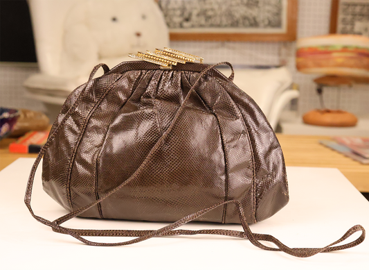 A brown Sharif El-Fouly lizard skin handbag with brass and crystal closure, displayed on a table.