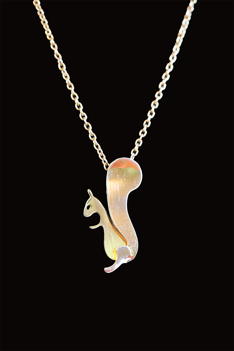 A gold-colored pendant in the shape of a squirrel on a chain against a black background.