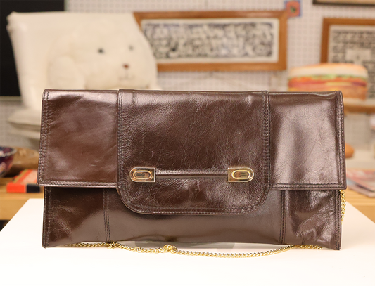 A dark brown Italian leather clutch with gold-tone hardware, a fold-over design, and a detachable chain strap.