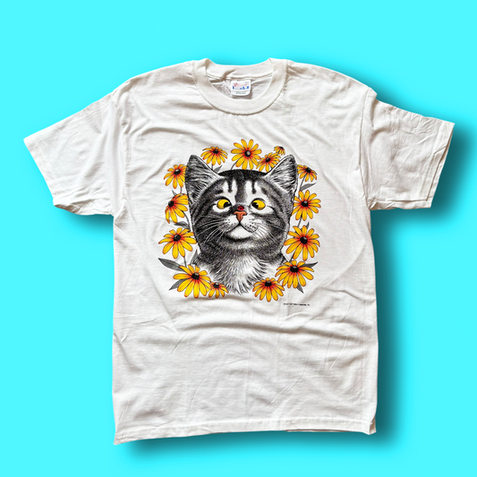 A beige t-shirt with a graphic print of a cat's face surrounded by flowers.