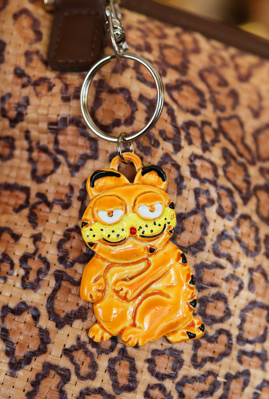 A keychain featuring an animated character resembling Garfield, in yellow and orange colors, sitting on a patterned surface.