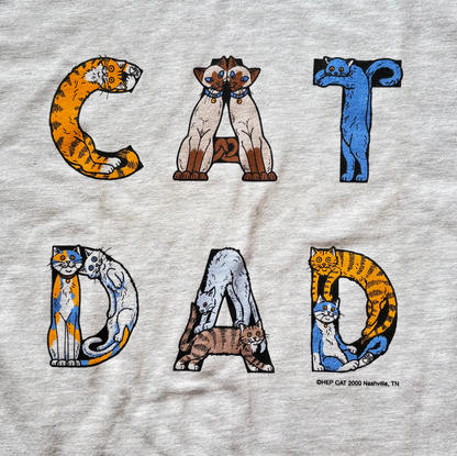 A gray t-shirt with the text 'CAT DAD' printed in bold letters, featuring a graphic of a cat face integrated into the design. Vintage Hep Cat tee