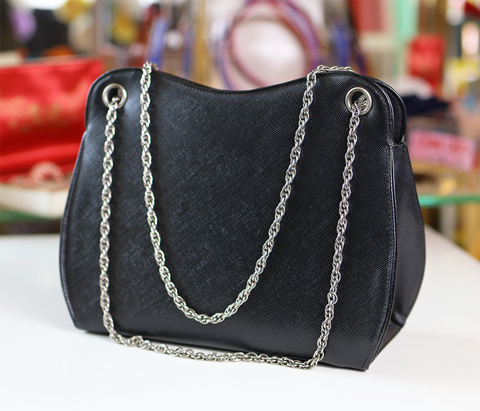 A handbag with a black leather body and silver chain straps, displayed against a blurred background.
