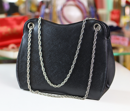 A handbag with a black leather body and silver chain straps, displayed against a blurred background.