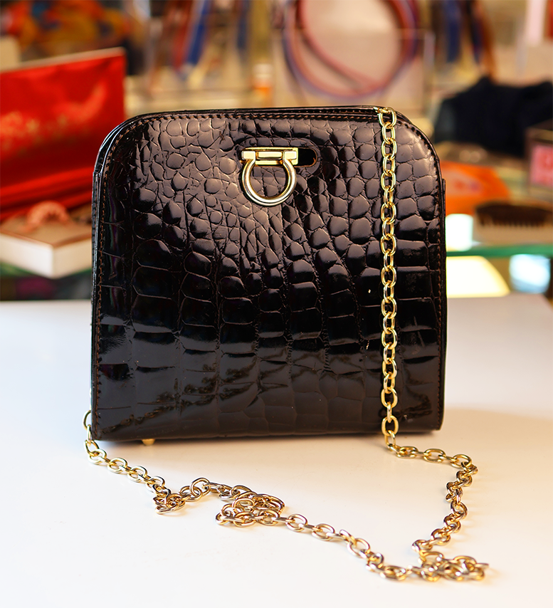 A small faux croc handbag with a black exterior and gold chain strap.