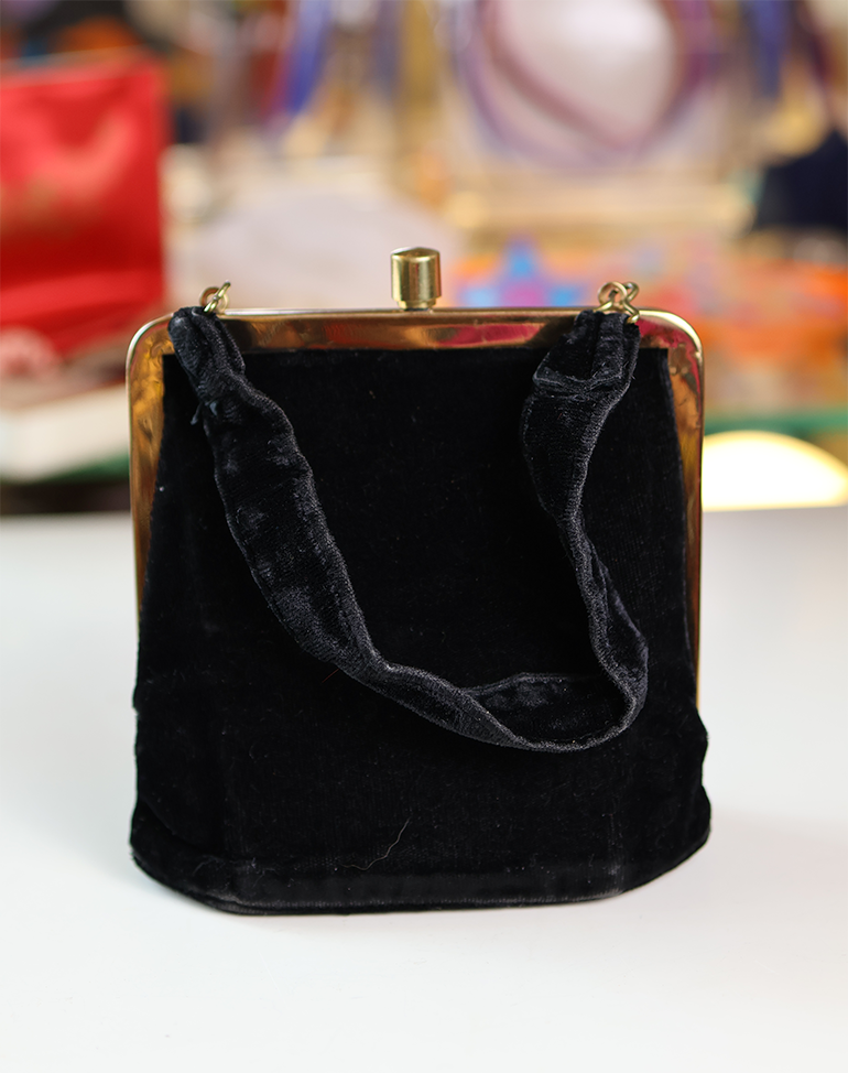 A black velvet handbag with a gold metal frame and a fabric handle.