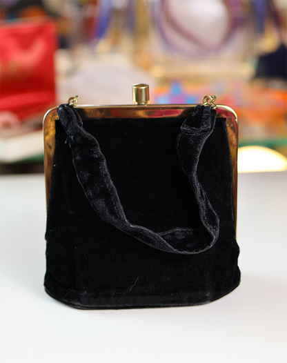 A black velvet handbag with a gold metal frame and a fabric handle.