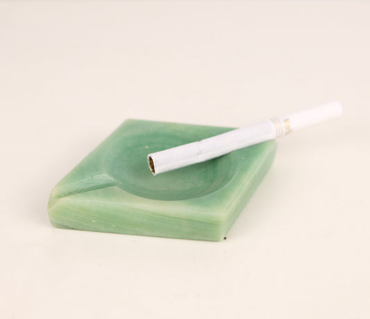 vintage 1930s art deco jade green onyx ashtray with a cigarette inside on a white background