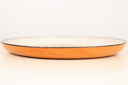 Orange ceramic plate with a white rim on a light beige background