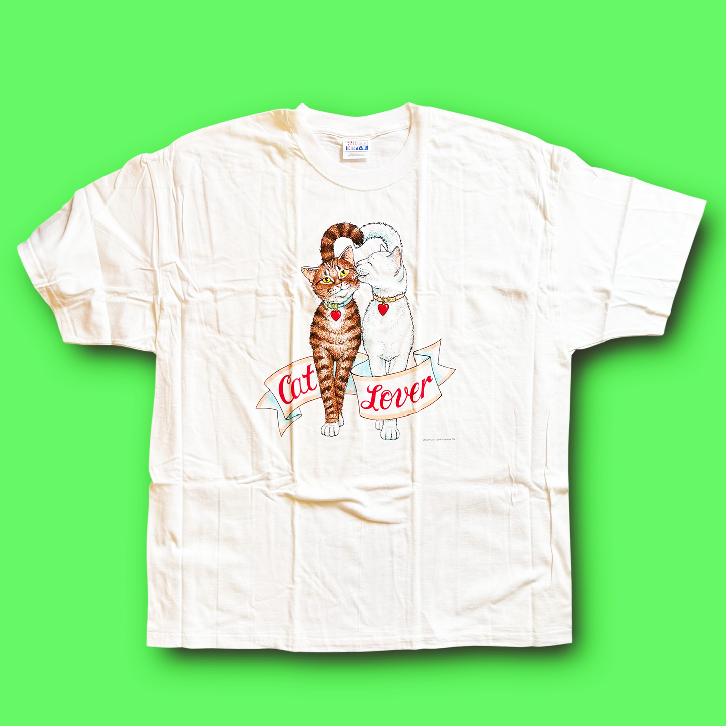 A white vintage t-shirt with a graphic of a cat and the text 'Cat Lover' on it, displayed against a green background.
