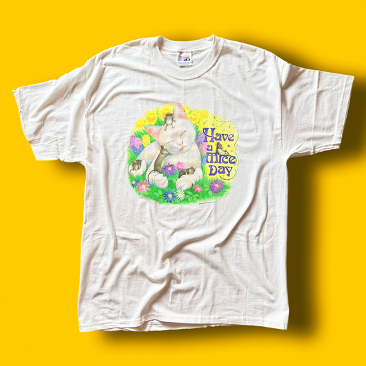 A white crew neck t-shirt with a graphic print in the center, featuring a cat, mice, and the text 'Have a Mice Day' on a yellow background.