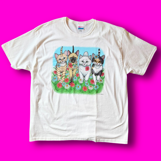 A graphic t-shirt featuring an illustration of four cats with flowers on a light-colored background.