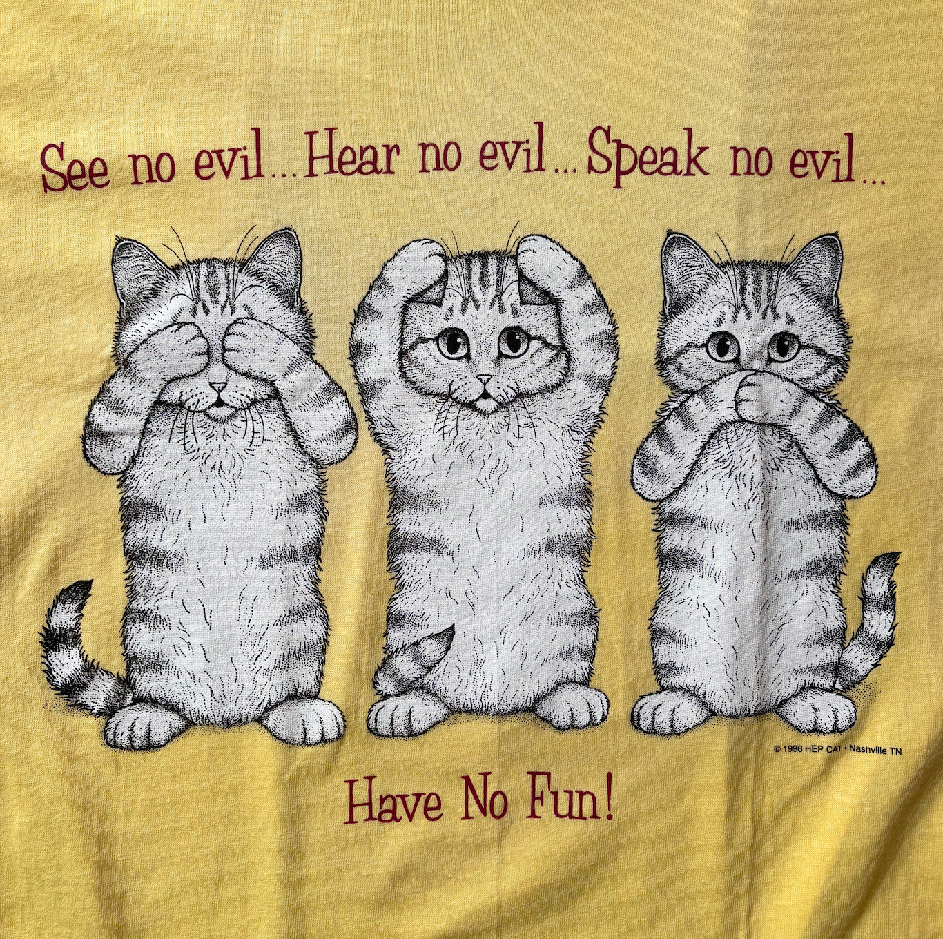 A yellow t-shirt with a graphic print of three cats and the text 'See no evil, Hear no evil, Speak no evil, Have No Fun!'