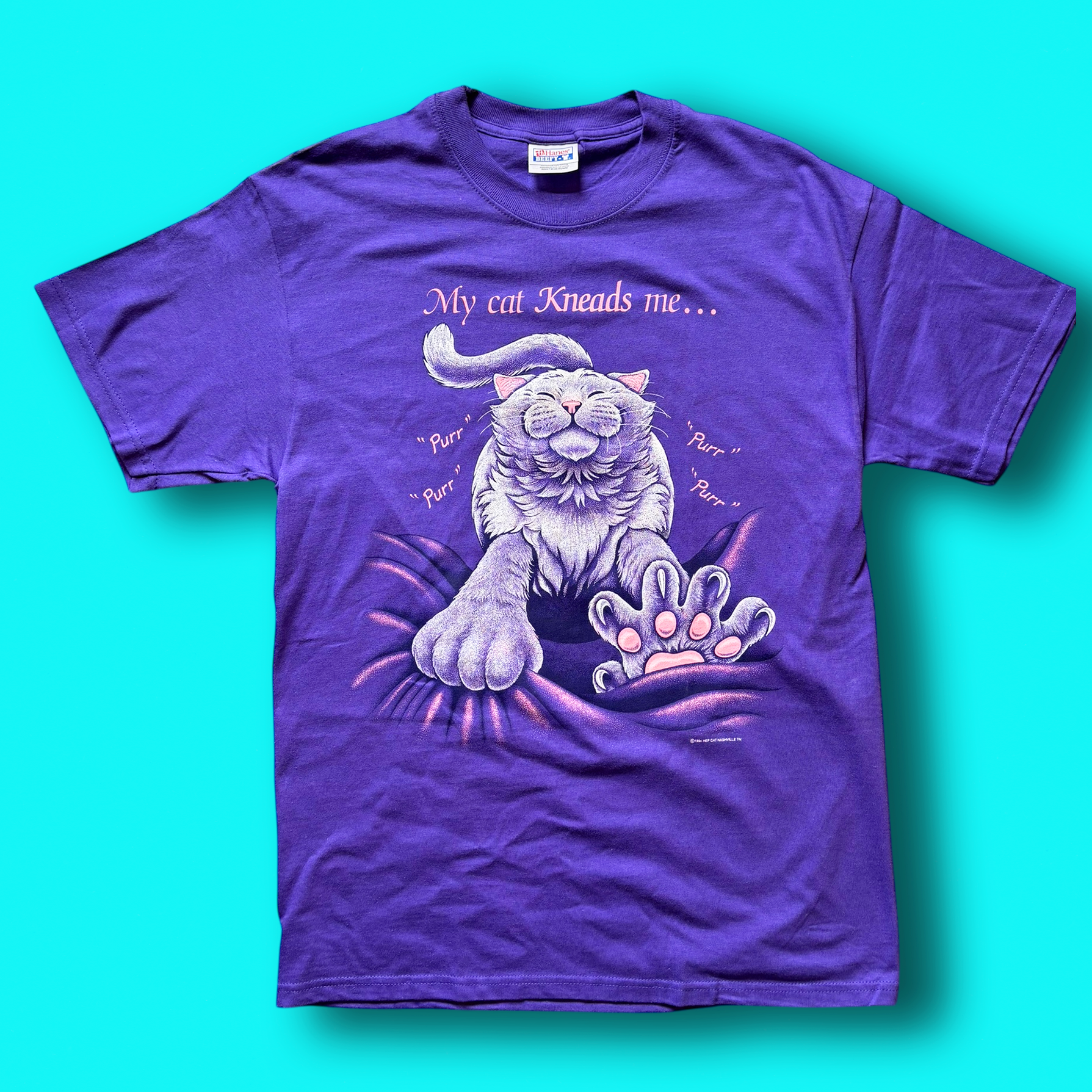 A purple t-shirt with a graphic print of a cat and the text 'My cat kneads me." Vintage Hep Cat Tee.