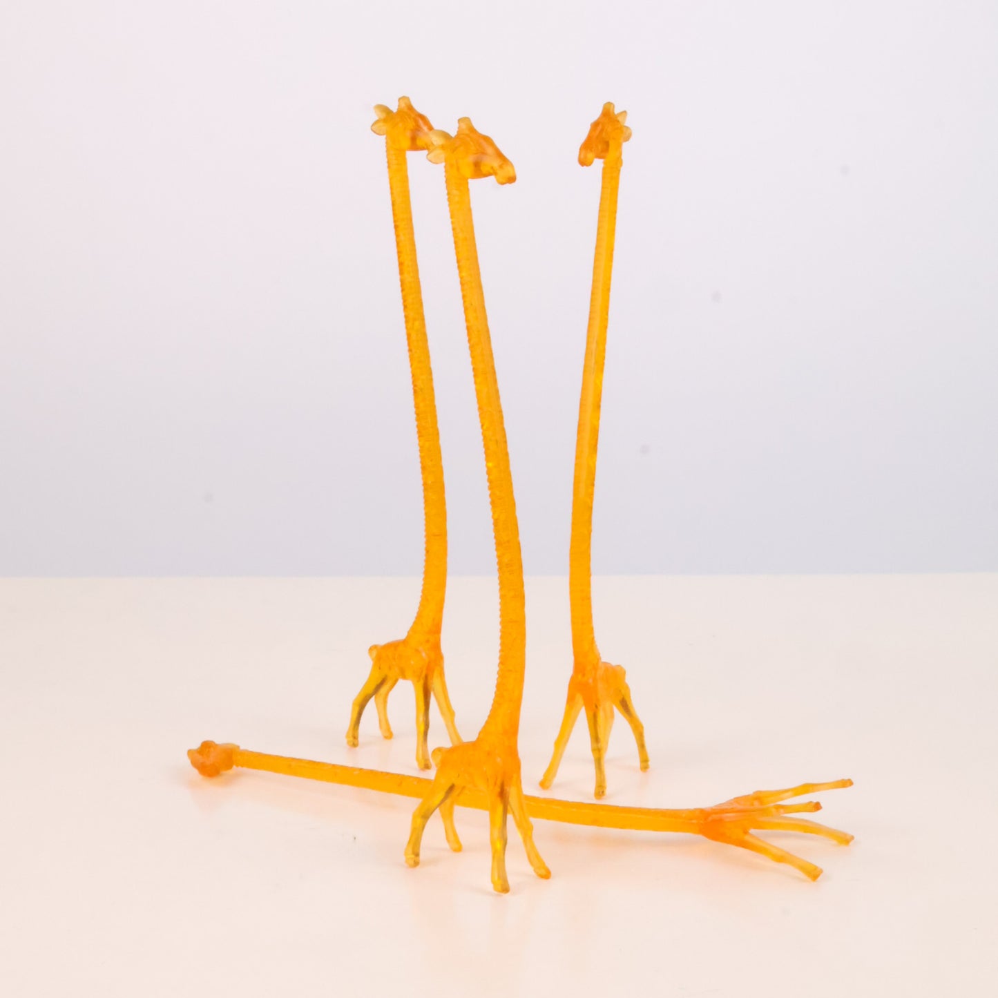 Four Vintage 1960s  orange giraffe-shaped stir sticks on a light gray background