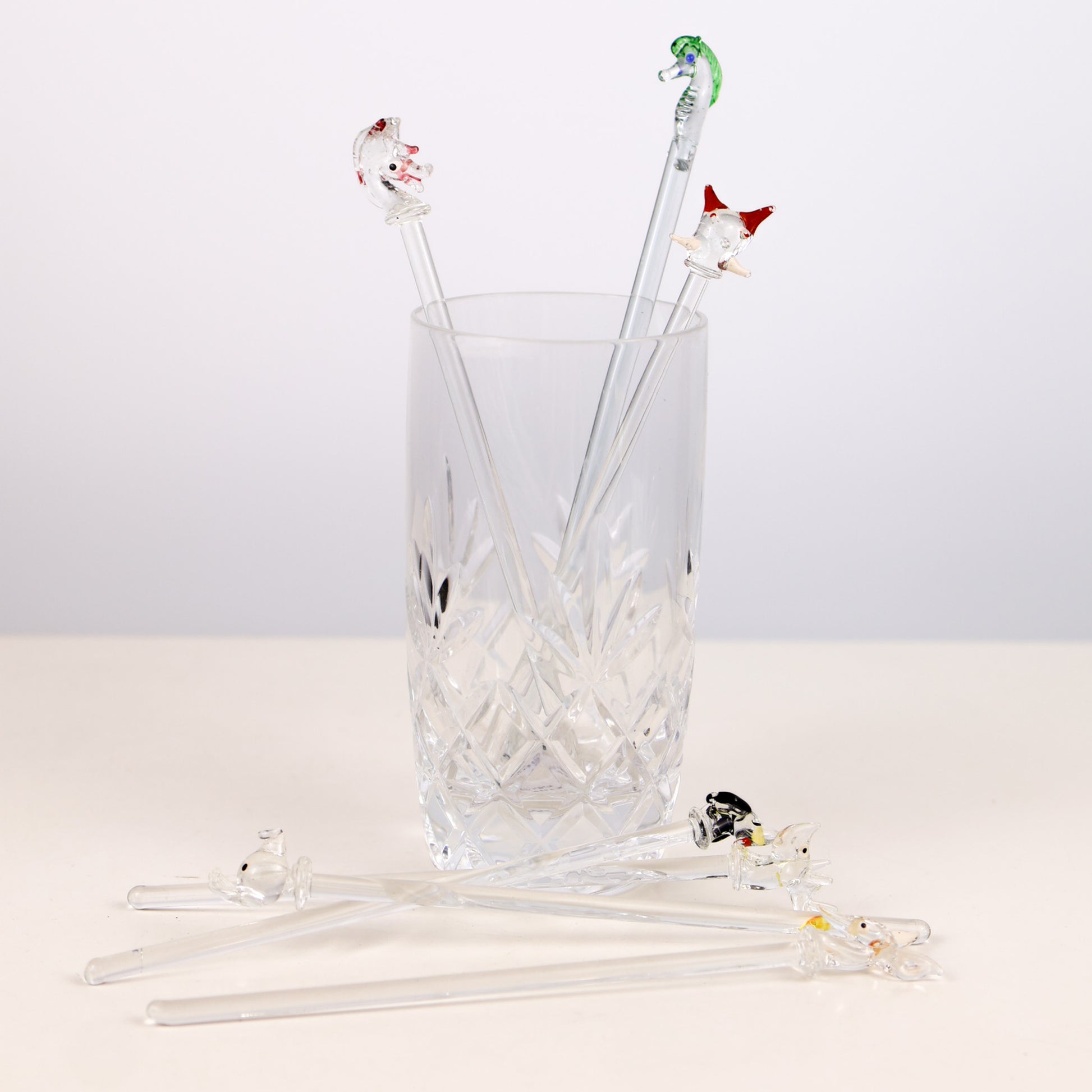 Set of glass swizzle sticks with animal ends in a clear glass on a white background