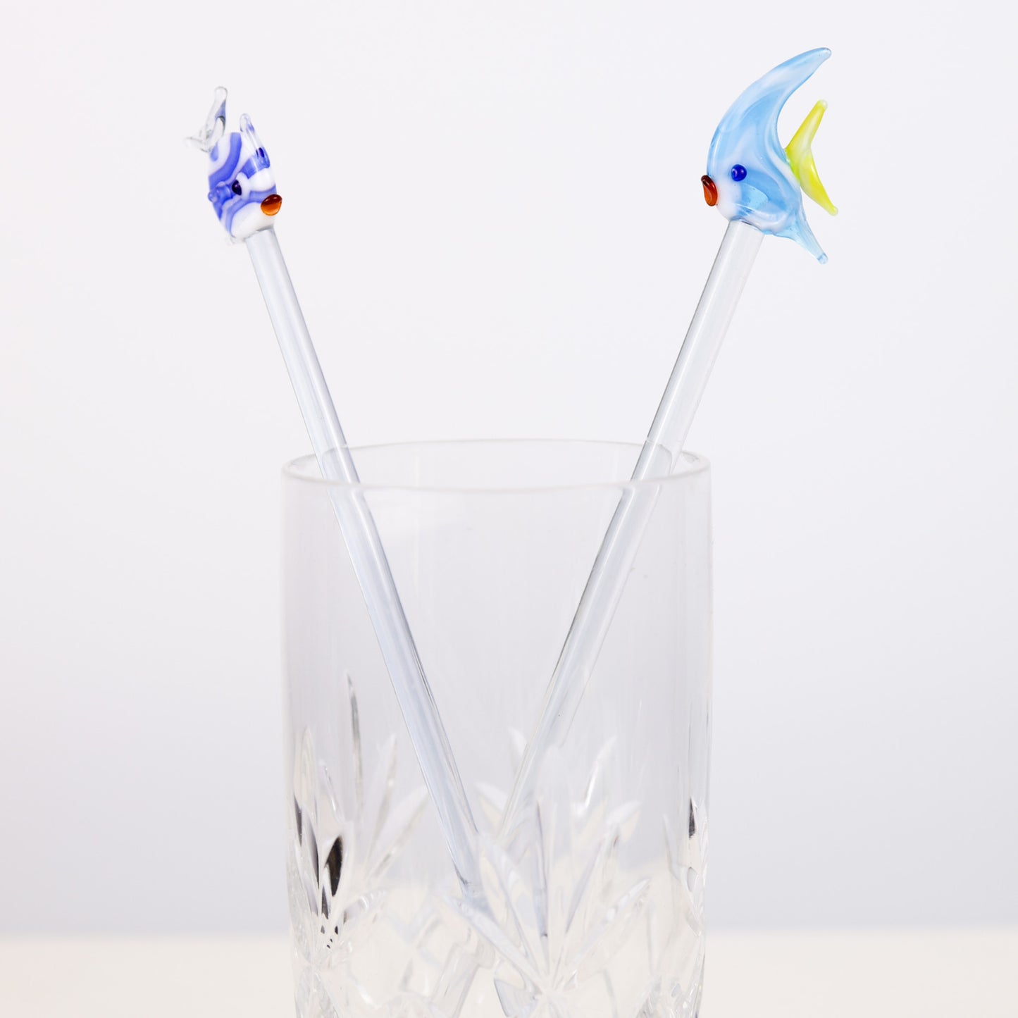 Two fish-shaped cocktail stirrers in a clear glass on a white background