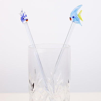 Two fish-shaped cocktail stirrers in a clear glass on a white background
