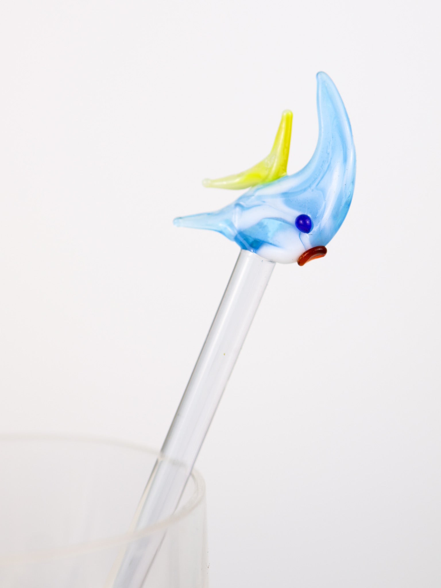 Glass fish swizzle stick with a blue body and colorful beak on a white background