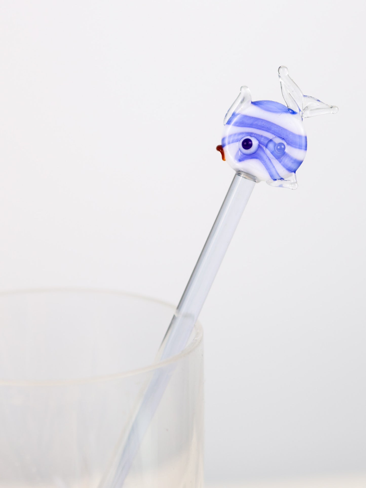 hand blown Glass swizzle stick  with a blue and white fish-shaped top on a light gray background
