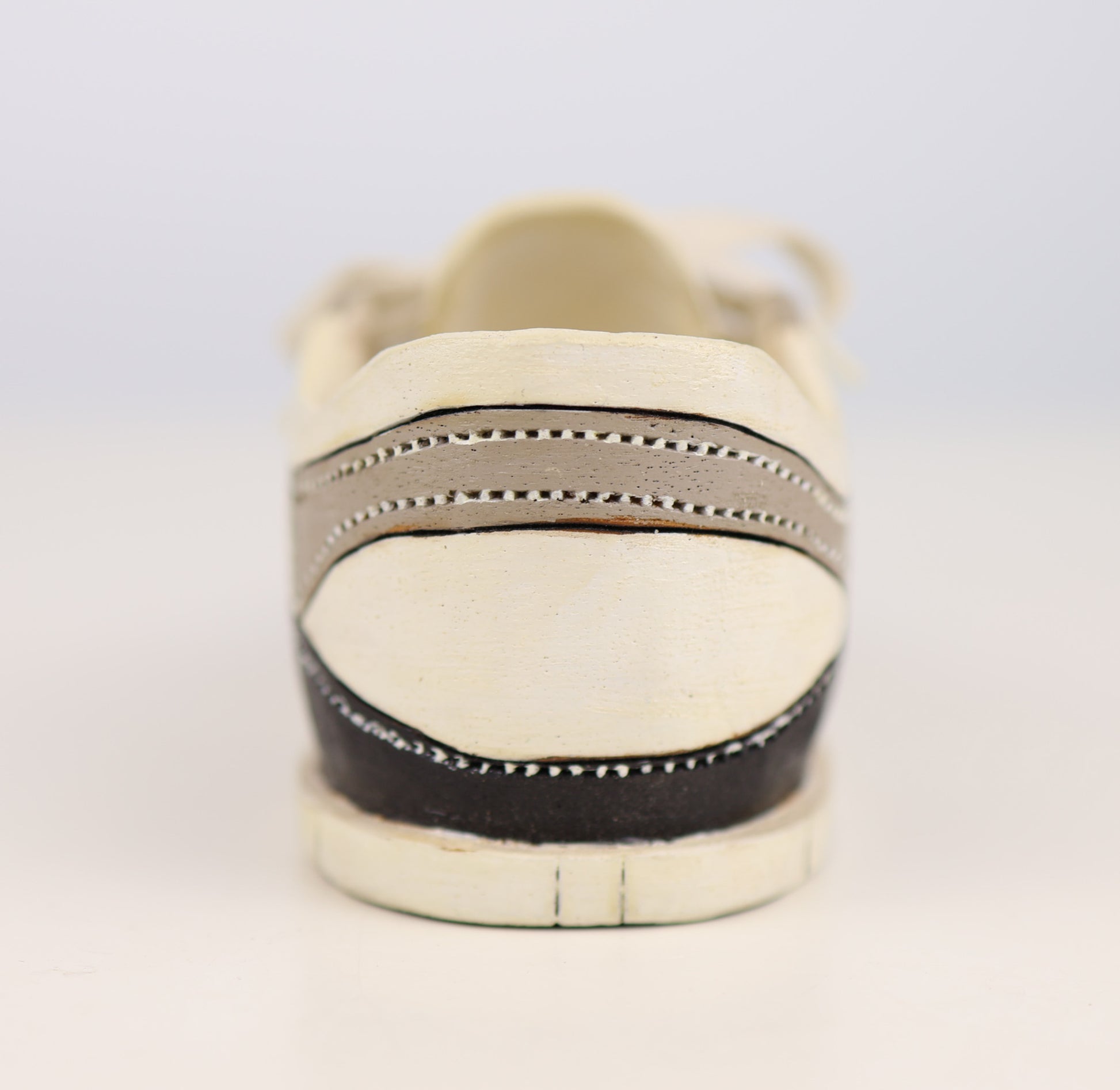 White sneaker with black sole on a light gray background